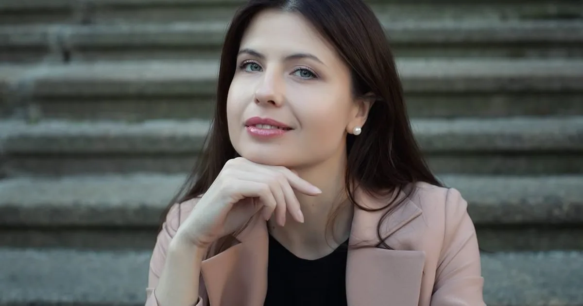 Жінка у світло-рожевому жакеті сидить на сходах і замислено дивиться вбік